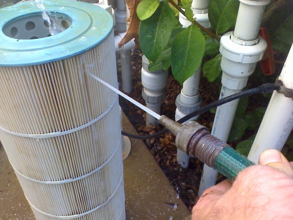 cartridge pool filter- with sand being washed out of it with a hose 